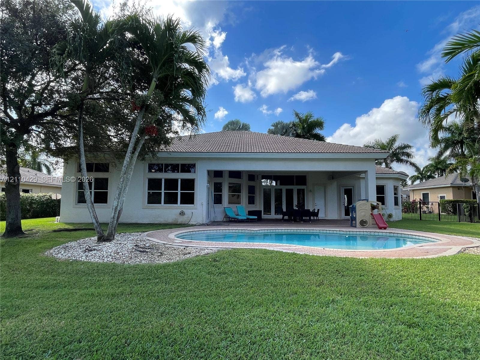 15001 SW 33rd Street, Davie, Davie, FL 33331 Rear exterior featuring a covered patio, swimming pool with decorative brick paver coping, expansive lawn, and mature palm trees