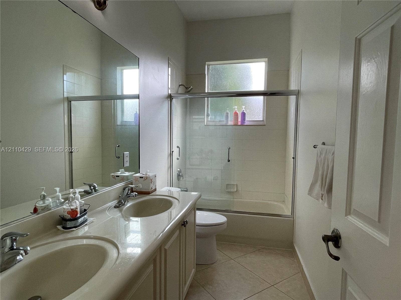 15001 SW 33rd Street, Davie, Davie, FL 33331 Dual-sink vanity with a molded countertop, large wall-mounted mirror, ceramic tile flooring, and a tub-shower combination featuring a sliding glass enclosure
