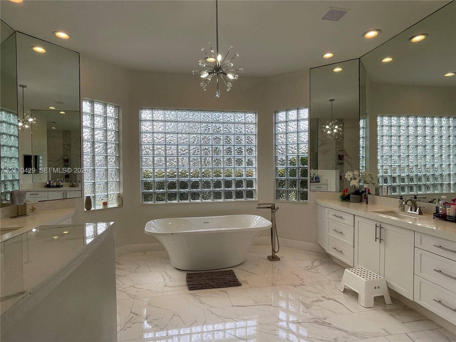 15001 SW 33rd Street, Davie, Davie, FL 33331 Freestanding soaking tub with floor-mounted faucet, dual white vanities with solid-surface countertops, large-format stone-patterned tile flooring, expansive glass block windows, and recessed lighting