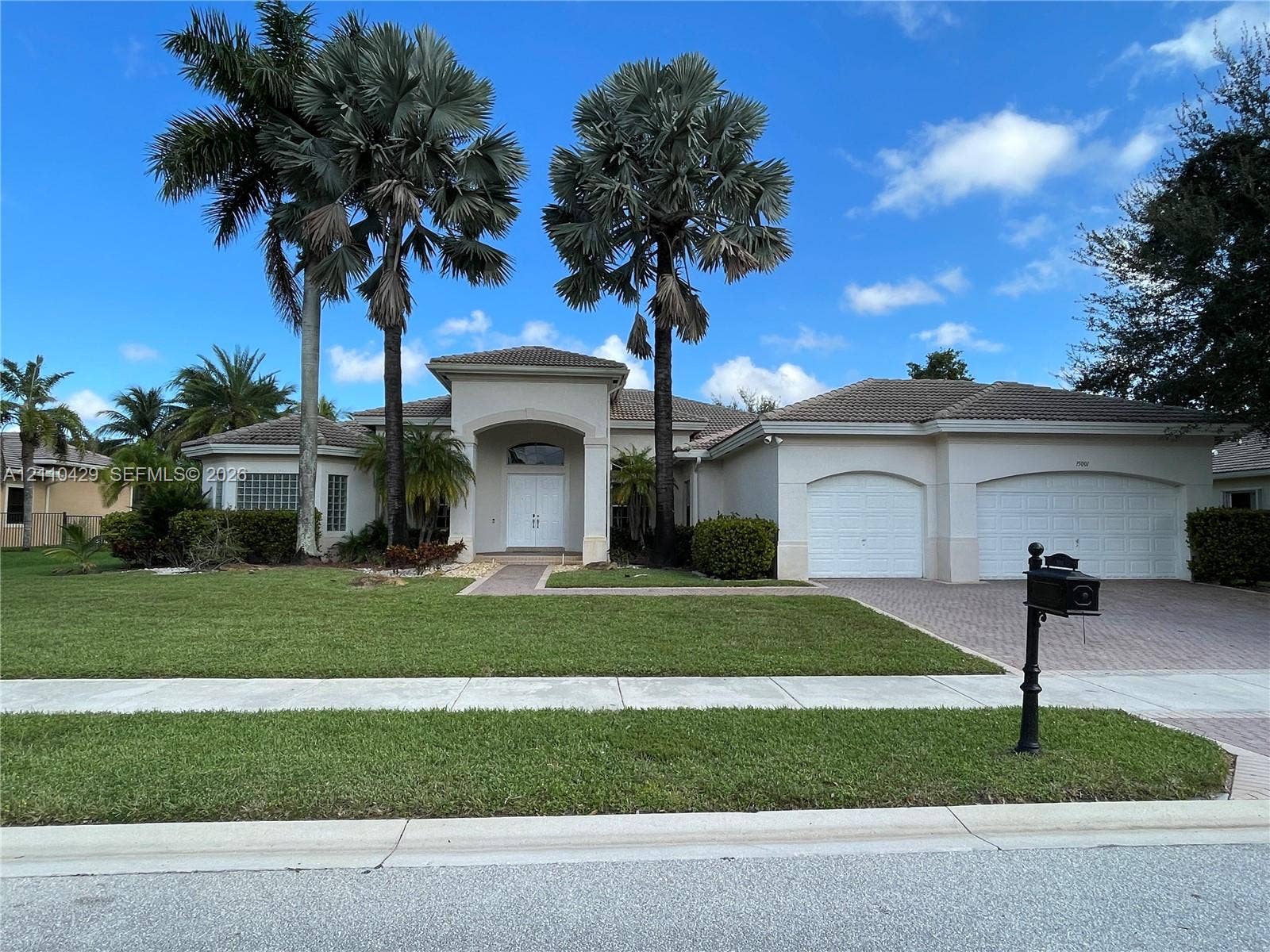 15001 SW 33rd Street, Davie, Davie, FL 33331 Stucco exterior residence featuring a covered entryway with arched roofline, dual-garage configuration, paver driveway, and mature palm trees