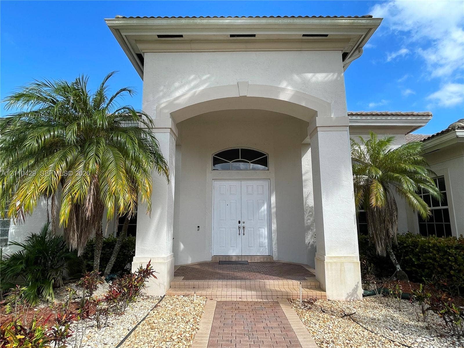 15001 SW 33rd Street, Davie, Davie, FL 33331 Stucco exterior featuring a covered entryway with architectural columns, a double-door entrance with an arched transom window, and a brick paver walkway