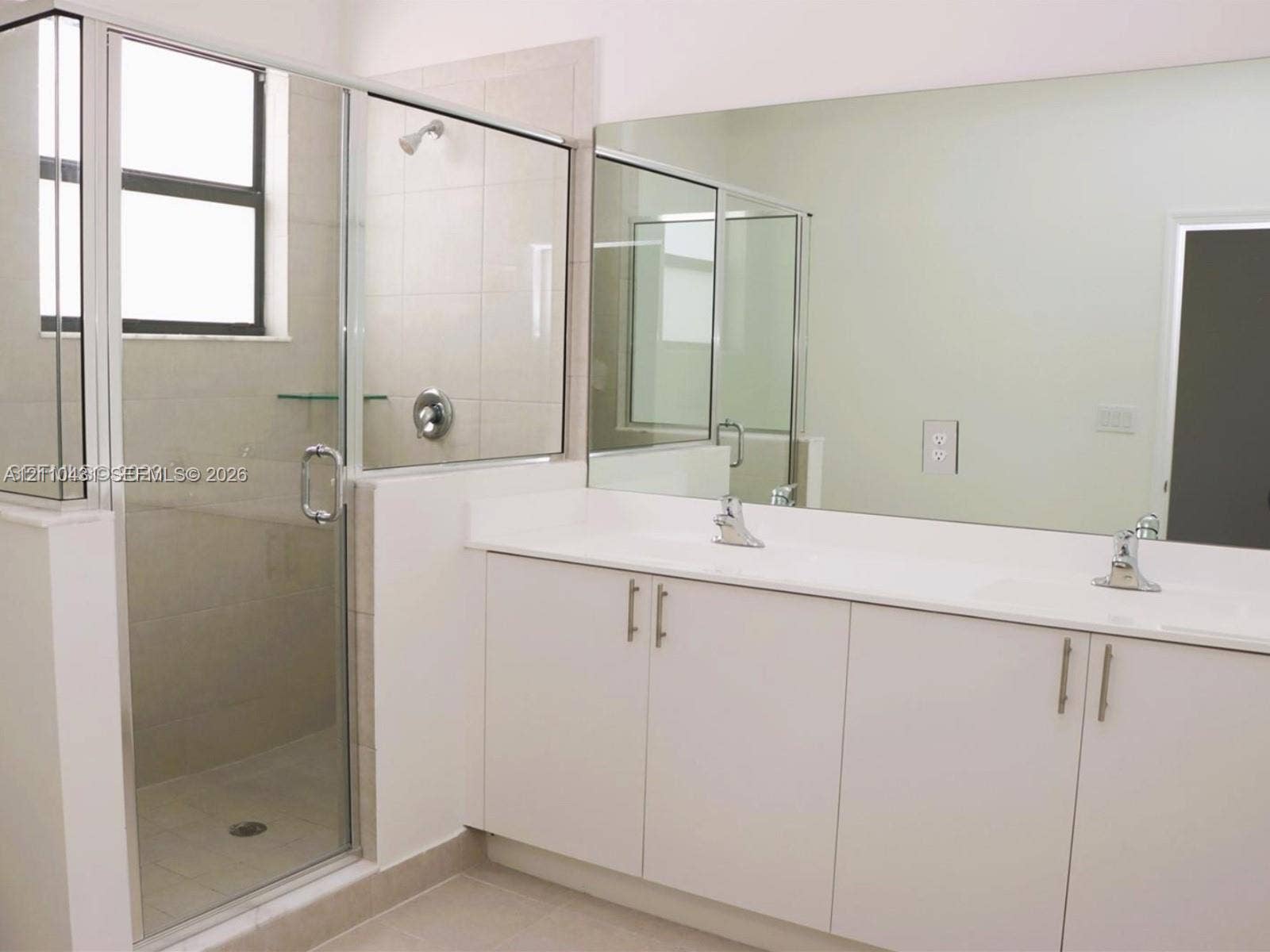 23452 SW 129th Avenue, Homestead, FL 33032 Double vanity with white cabinetry, solid-surface countertop, dual integrated sinks, and polished chrome faucets, complemented by a walk-in shower with glass enclosure and full-width mirror