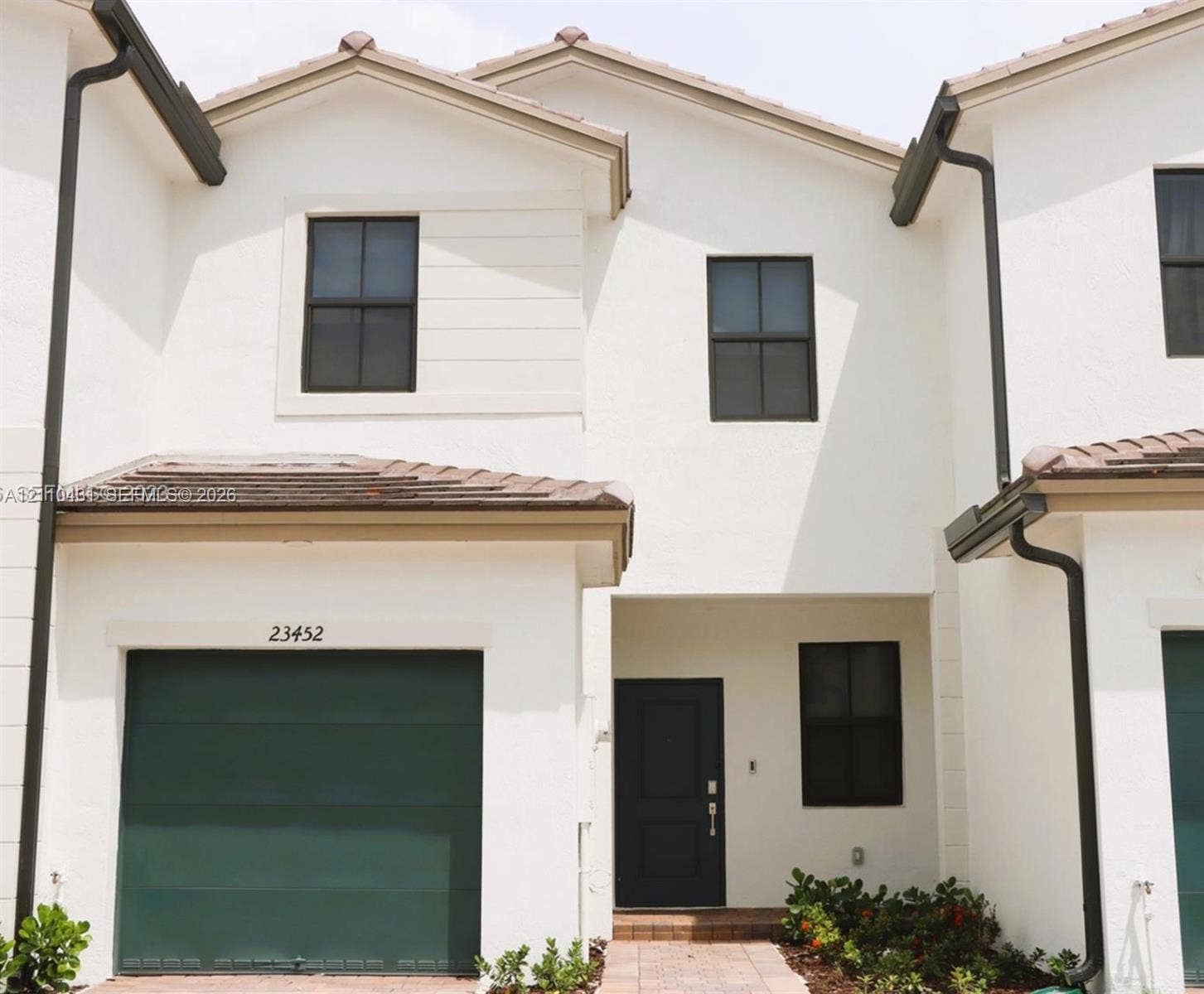 23452 SW 129th Avenue, Homestead, FL 33032 Exterior featuring a stucco facade, dark-toned garage door, gabled roofline, dark-framed multi-pane windows, and a paved entryway path