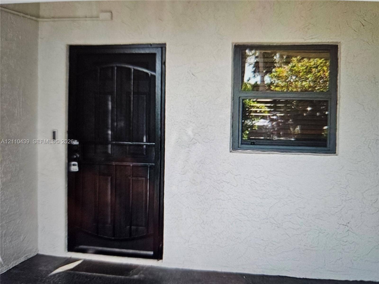 Entryway featuring a dark-finish security storm door, textured stucco exterior wall, and a single-hung window with dark-toned framing