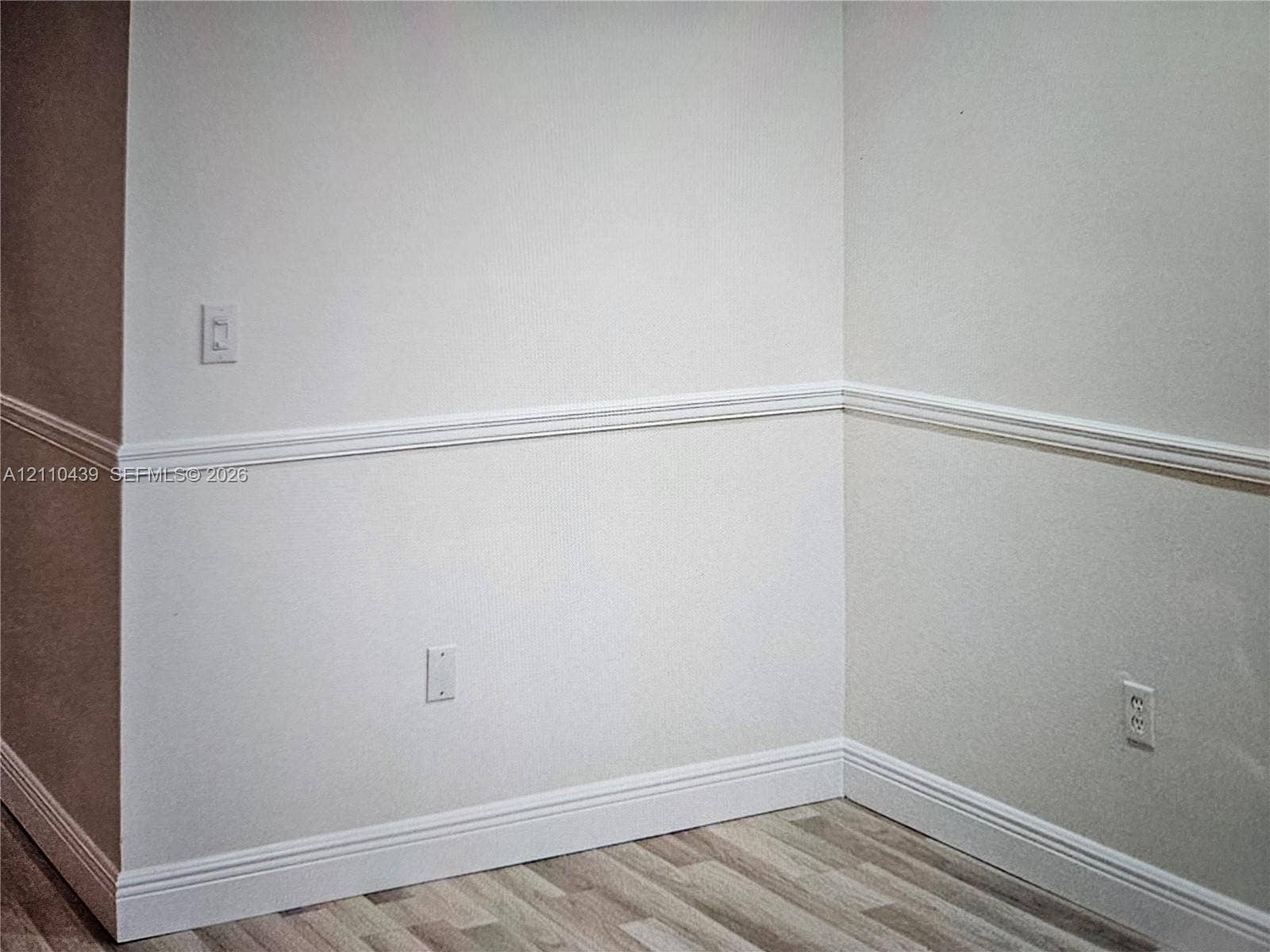 Interior corner featuring neutral wall paint, white chair rail molding, and wood-finish flooring