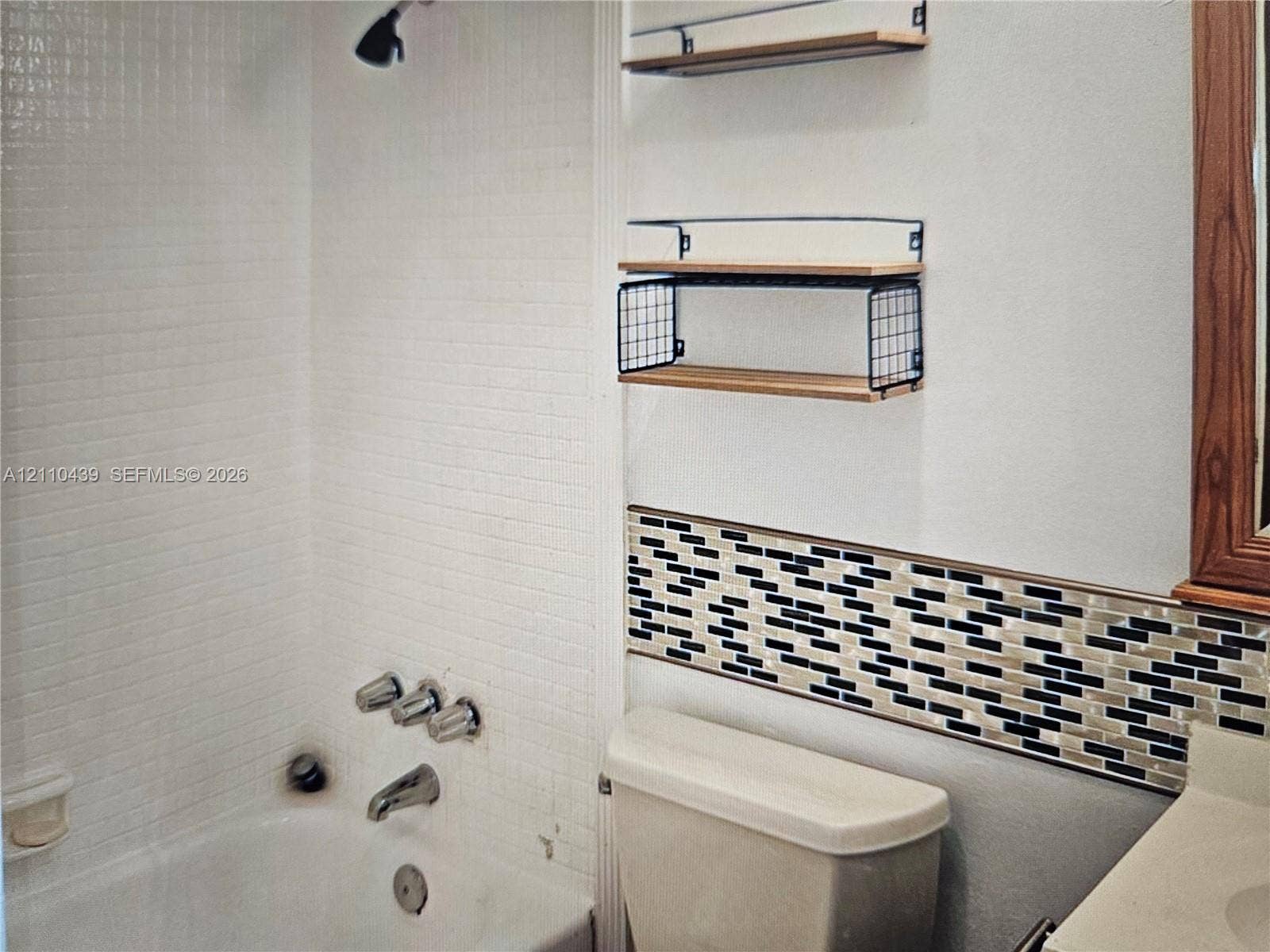 Shower and tub combination featuring small-format white tile surround, mosaic tile backsplash, and mounted wood and metal shelving