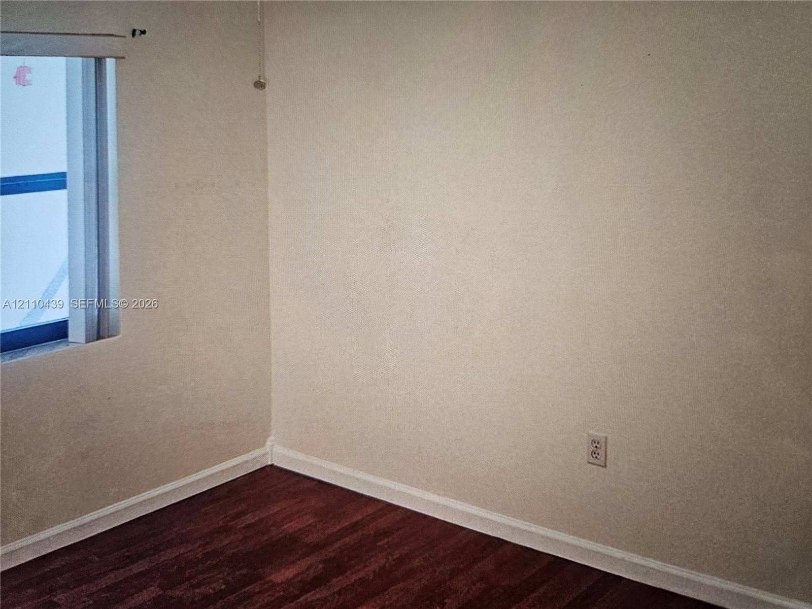Room featuring wood-finish flooring, neutral-toned walls, and a single-pane window with a roller shade
