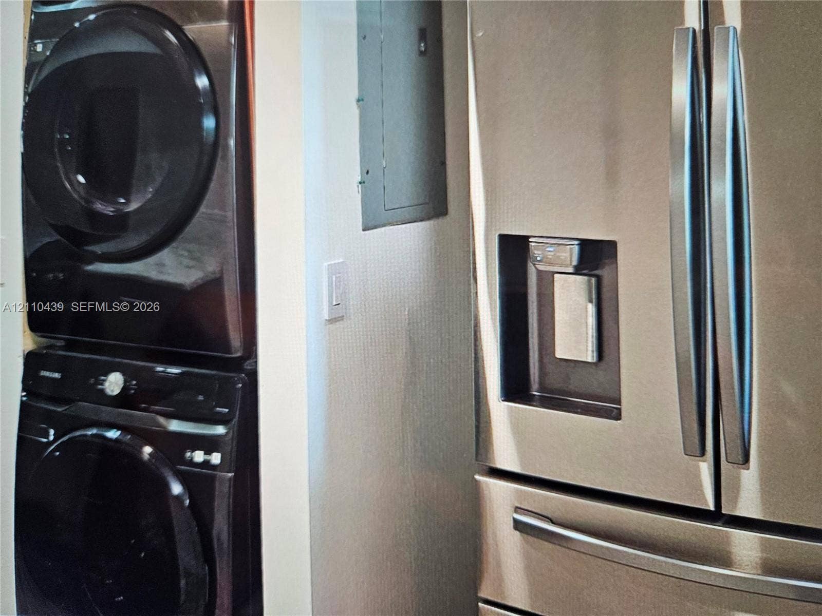 Stacked washer and dryer unit, stainless steel French door refrigerator with integrated water and ice dispenser, and wall-mounted electrical panel