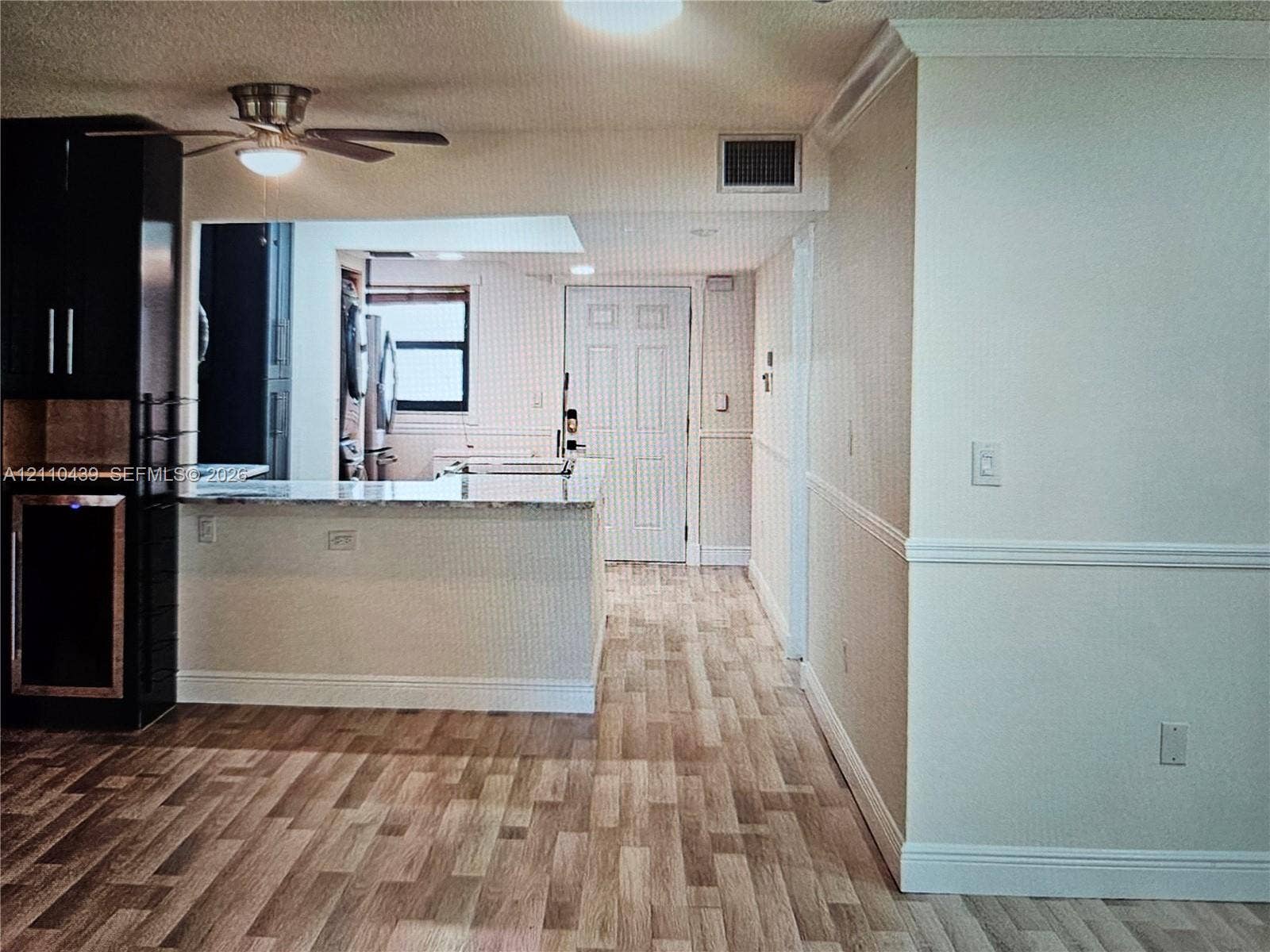 Wood-finish flooring, dark cabinetry with built-in wine cooler, stone-surfaced peninsula, and ceiling fan with integrated lighting