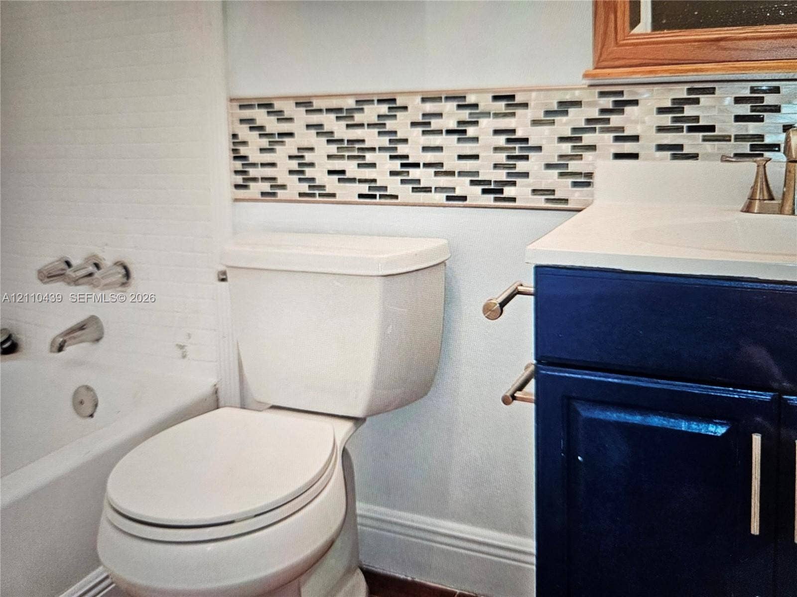 Navy blue vanity with light-toned solid surface countertop, decorative horizontal mosaic wall tile, and polished metal plumbing fixtures