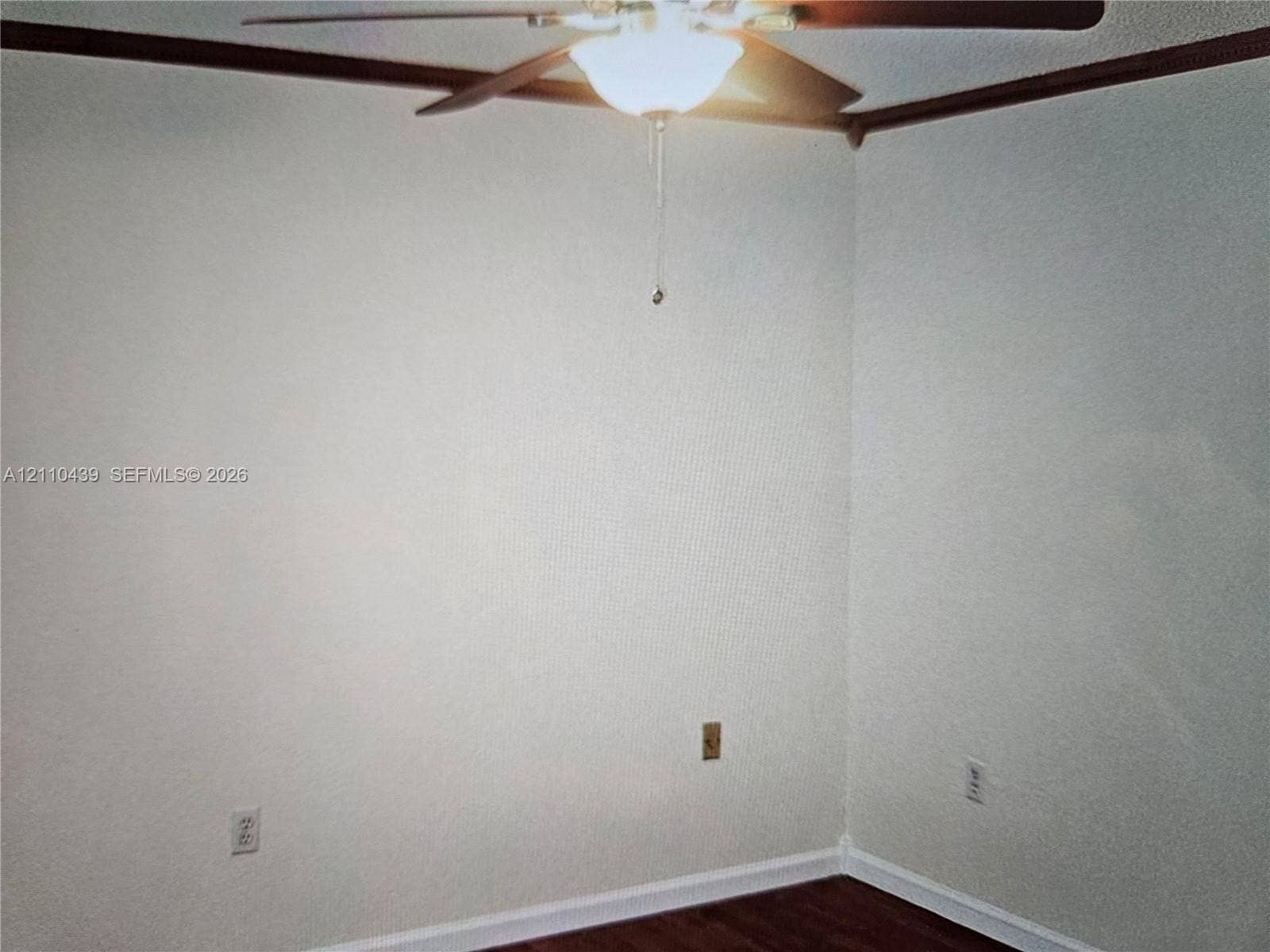Room featuring wood-finish flooring, textured walls, and a ceiling-mounted fan with integrated light fixture