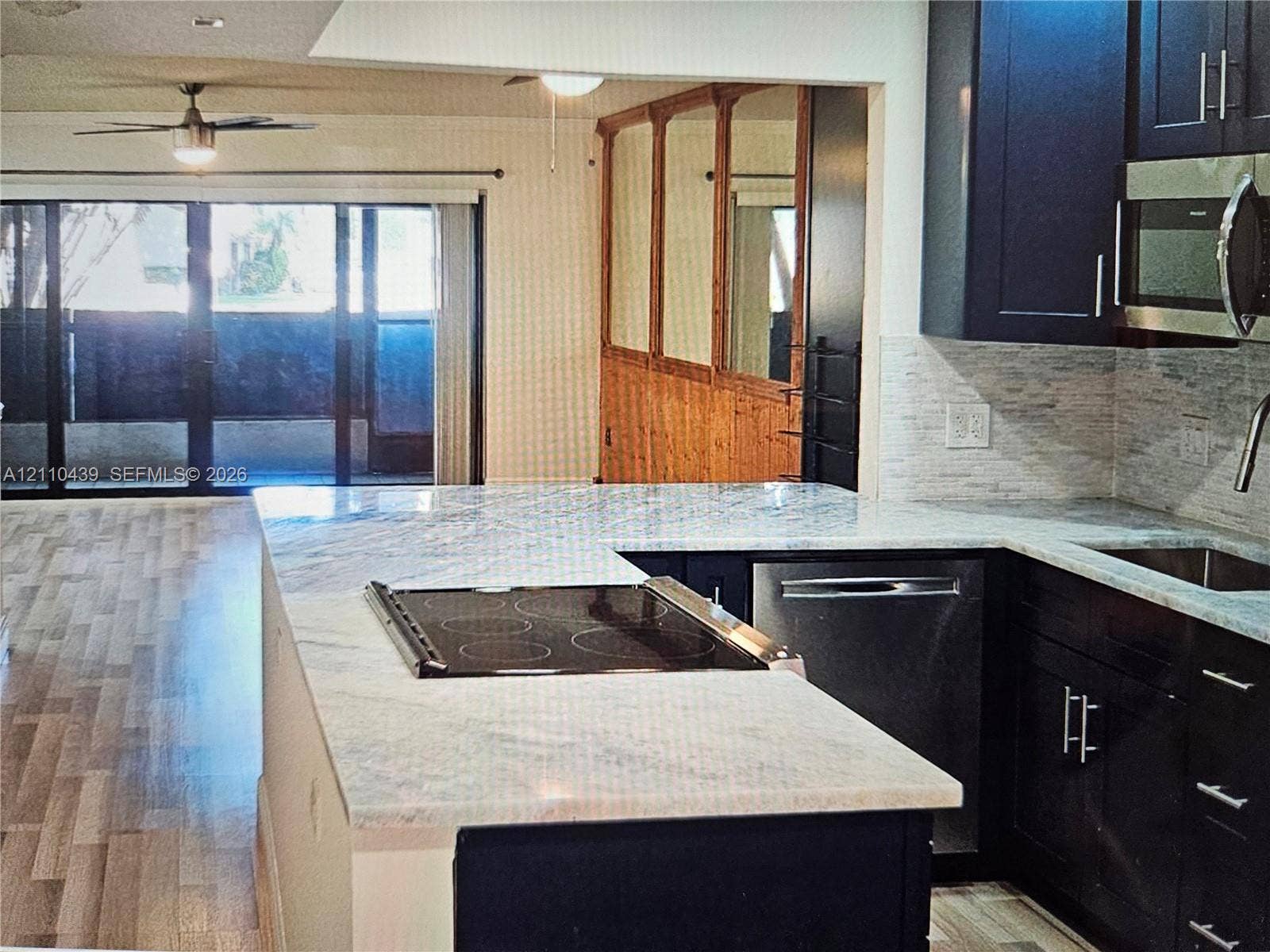 Kitchen featuring dark cabinetry, stone countertops, an integrated glass cooktop, stainless steel dishwasher, and stacked-stone backsplash