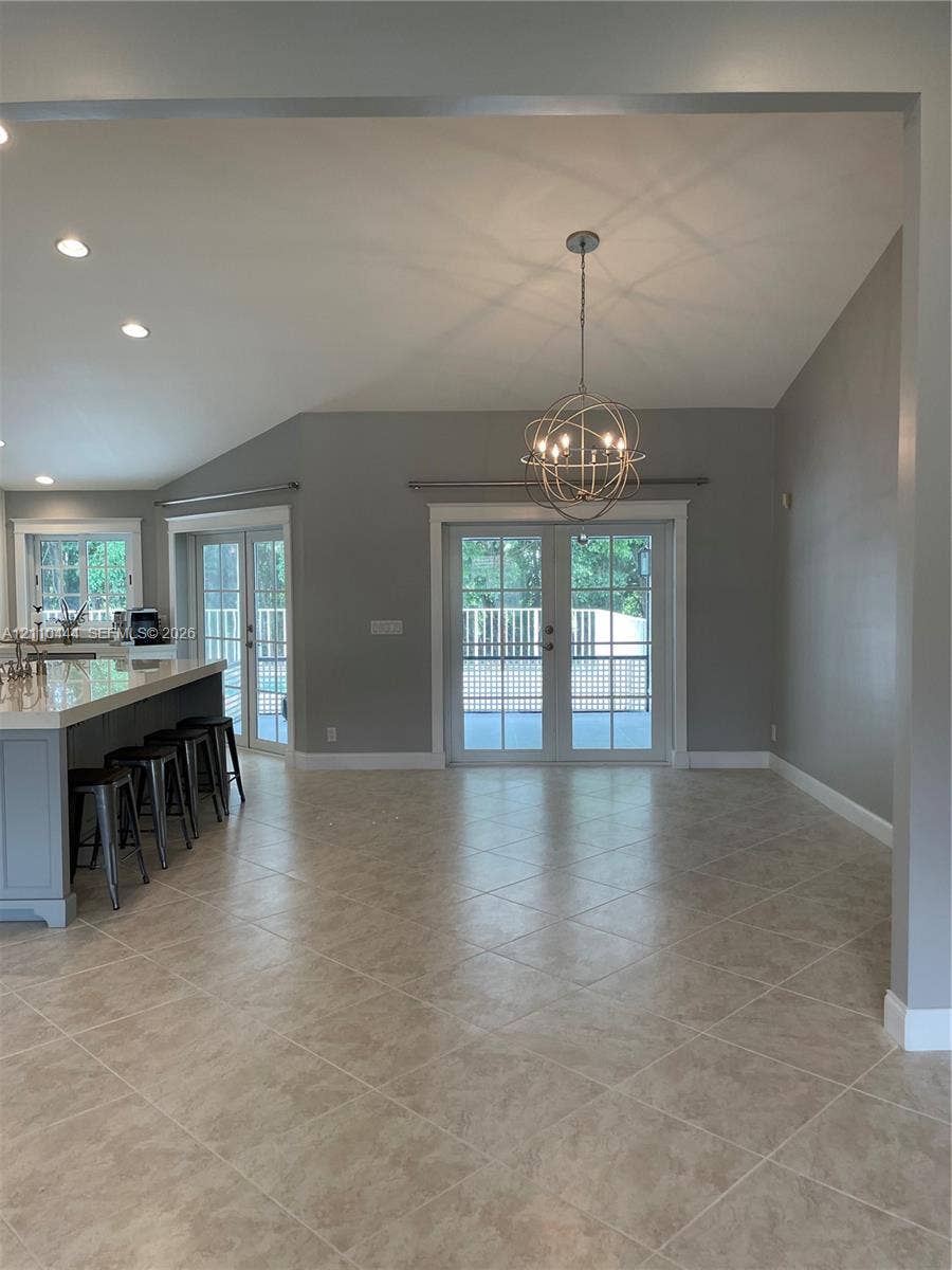 Open-concept interior featuring vaulted ceilings, tile flooring set on a diagonal, a kitchen island with a stone-finish countertop, a spherical metal chandelier, and French doors
