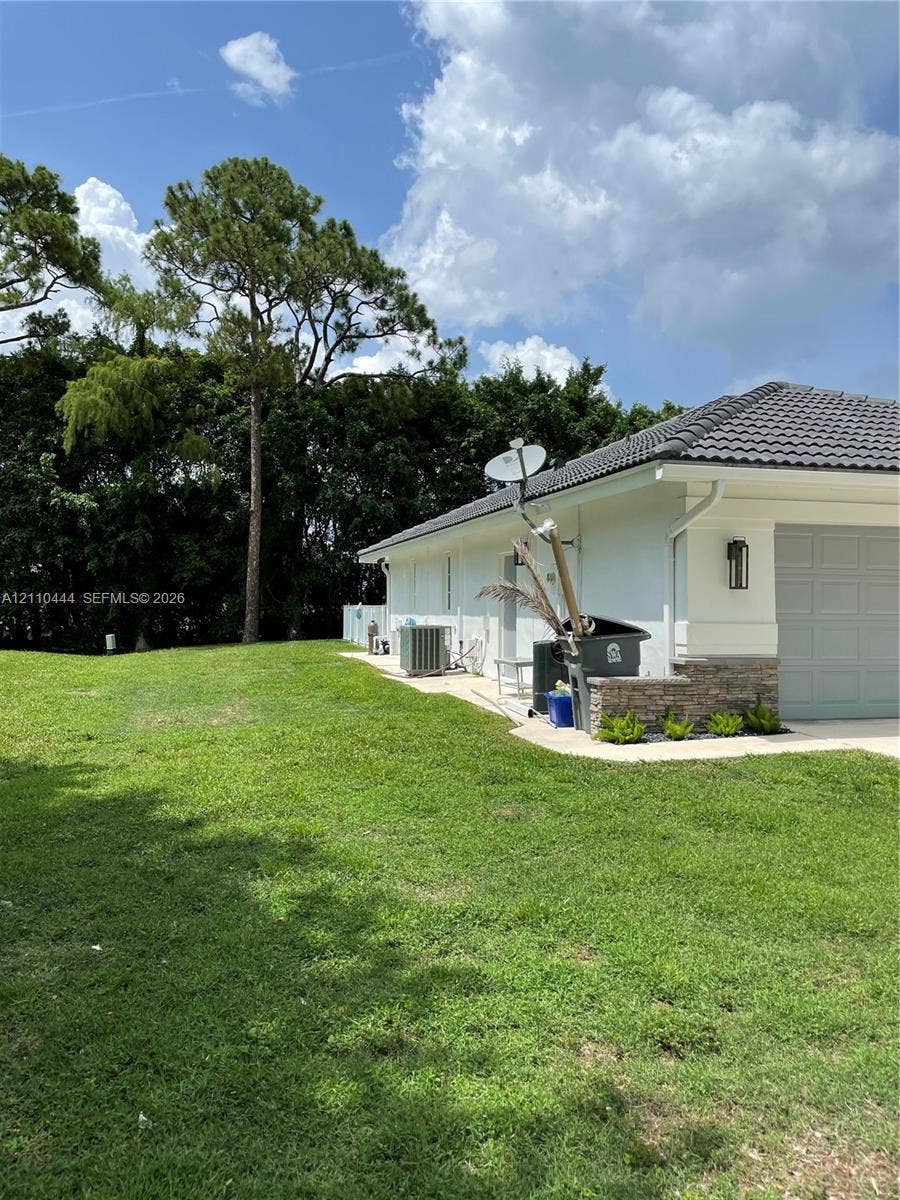 Expansive side yard featuring a manicured lawn, stone-veneer exterior accents, tile roofing, and mature perimeter trees
