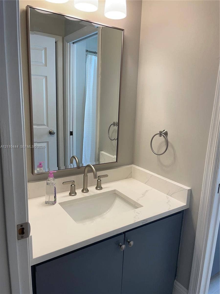 Bathroom vanity featuring a stone-composite countertop with integrated sink, polished chrome widespread faucet, navy blue cabinetry, and a framed rectangular wall mirror