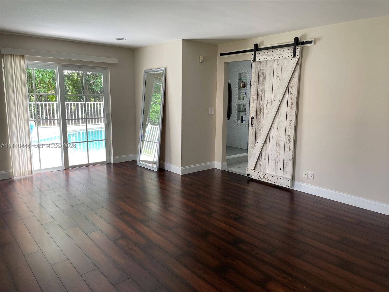 Dark wood-finish flooring, sliding glass door with exterior pool access, and distressed white-finish barn door with matte black hardware
