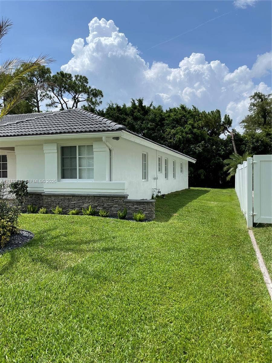 Stucco exterior featuring stone masonry accents, a tiled roof, multi-pane windows, and a fenced yard with a manicured lawn