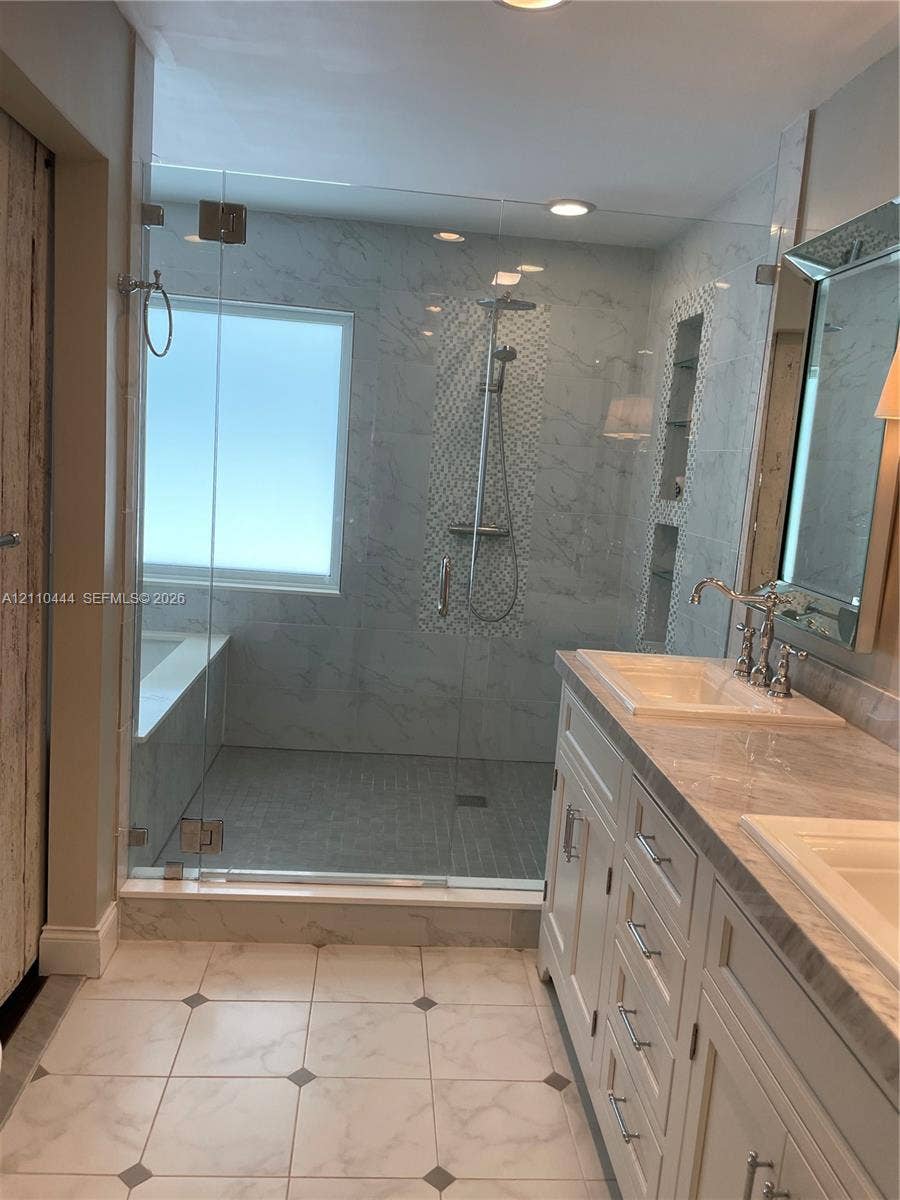 Walk-in shower featuring glass paneling, floor-to-ceiling tile, and built-in shelving, paired with a dual-sink vanity with stone-finish countertops and polished metal fixtures