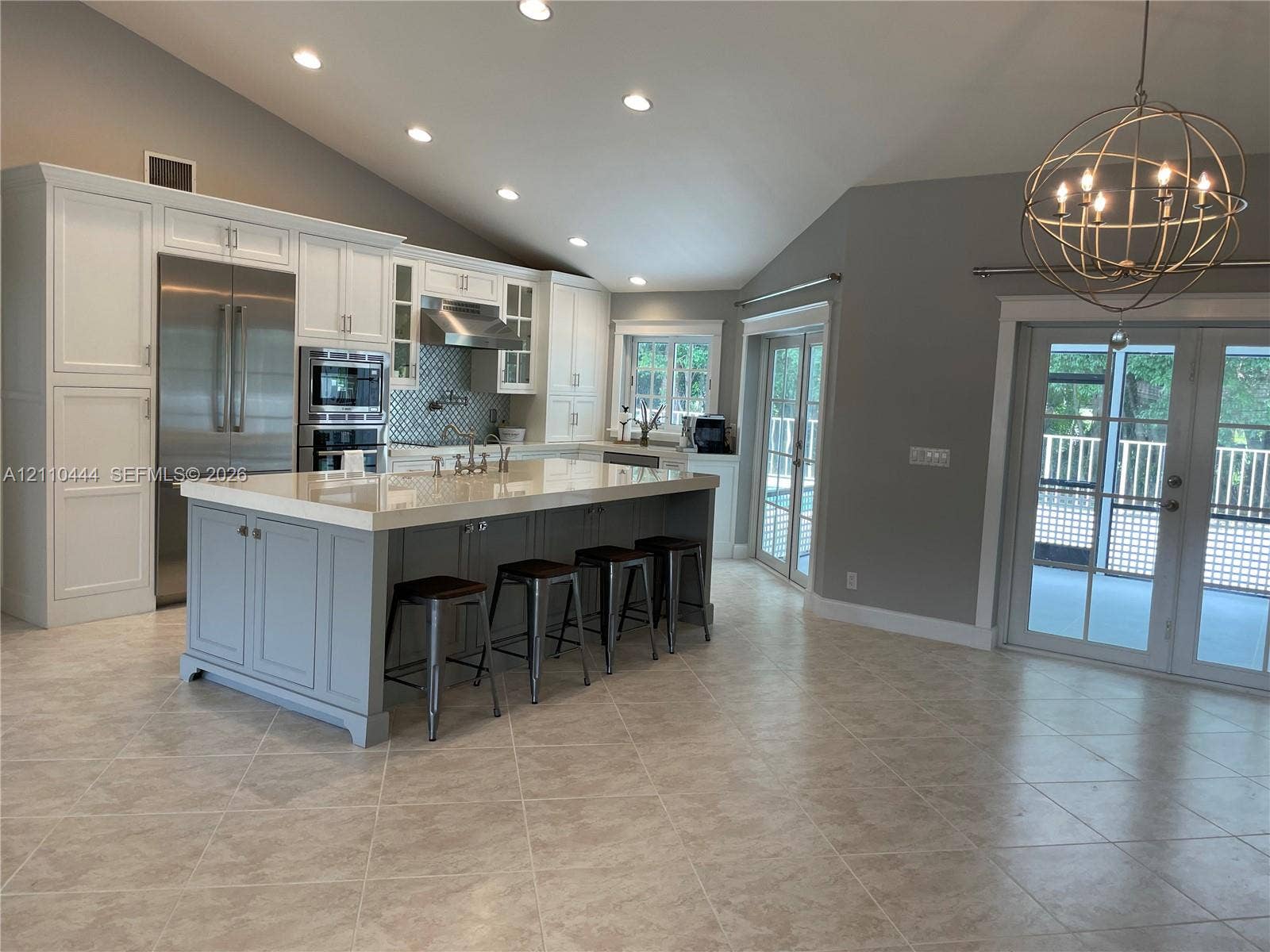 Kitchen featuring an oversized central island with stone-finish countertops, stainless steel appliances, vaulted ceilings, recessed lighting, and glass-paned doors