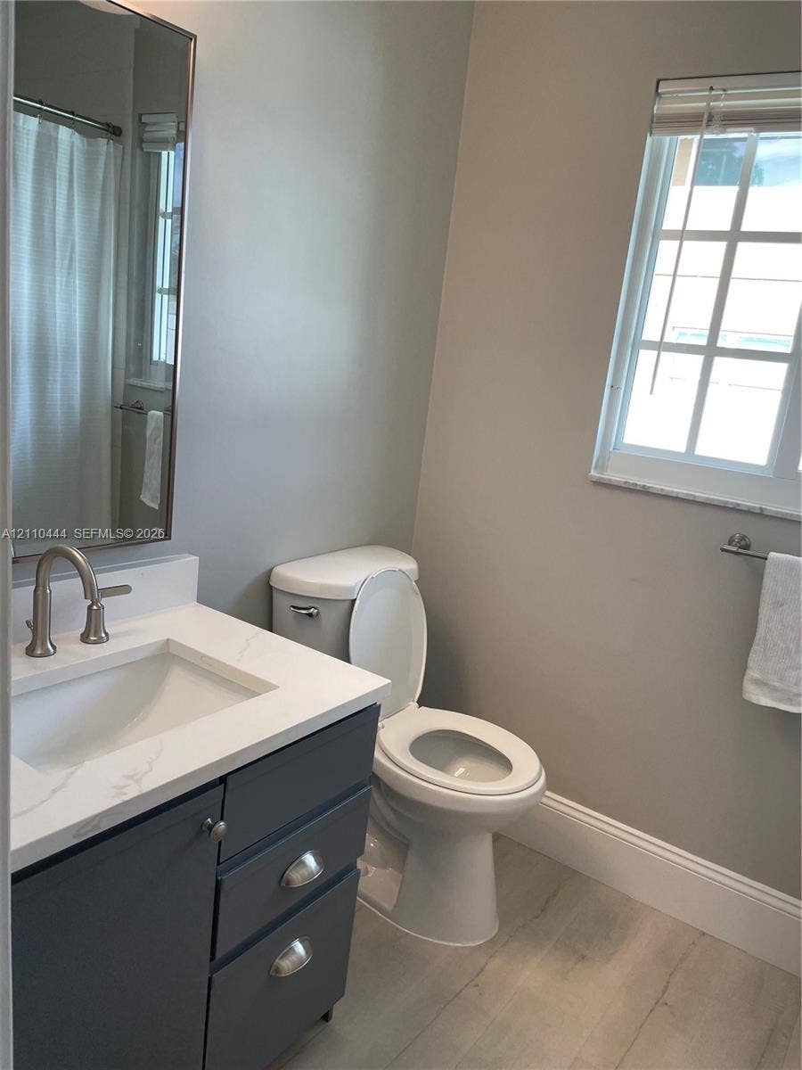 Bathroom featuring a vanity with dark cabinetry, stone-finish countertop, undermount sink, and arched-spout faucet, complemented by wood-finish flooring and a multi-pane window
