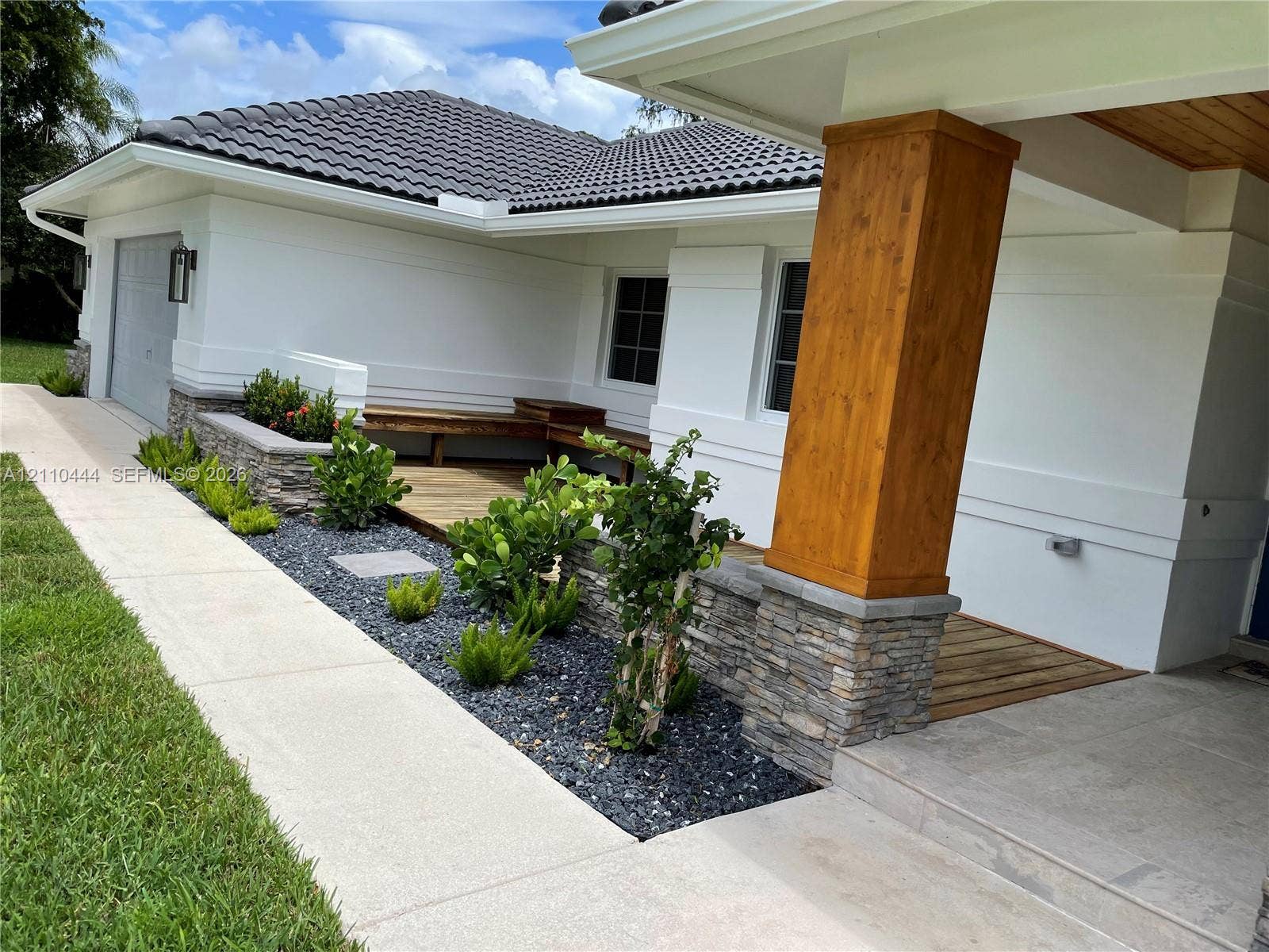 Exterior facade featuring a concrete tile roof, stone masonry accents, a wood-finish support column, and built-in wood decking with integrated bench seating