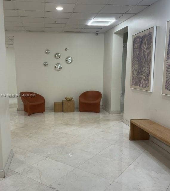 2780 NE 183rd Street, #517, Aventura, FL 33160 Polished stone flooring in a diagonal tile pattern, drop ceiling with integrated recessed lighting, and wall-mounted security fixtures