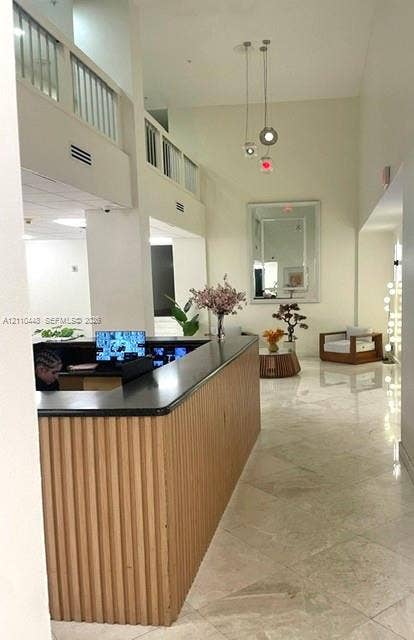 2780 NE 183rd Street, #517, Aventura, FL 33160 High-ceilinged foyer featuring a built-in reception desk with a ribbed wood-finish base and dark stone countertop, polished tile flooring, and a multi-pendant light fixture