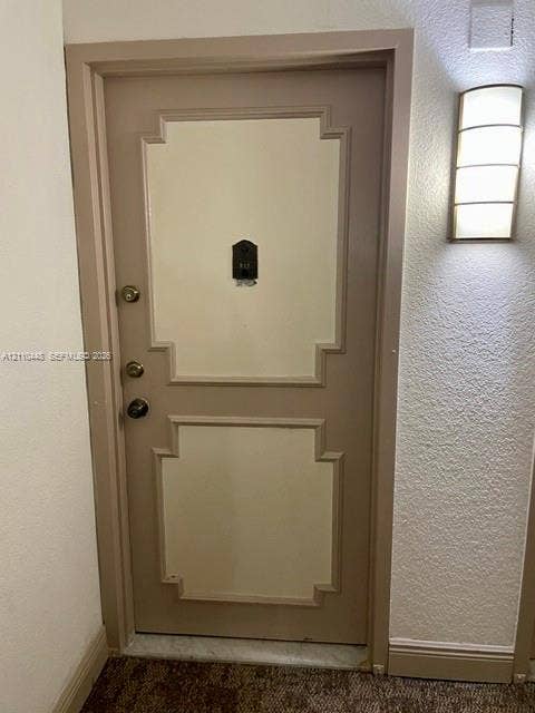 2780 NE 183rd Street, #517, Aventura, FL 33160 Solid core door with decorative recessed panel detailing, integrated metal peephole, brass-finished hardware, and wall-mounted arched glass sconce
