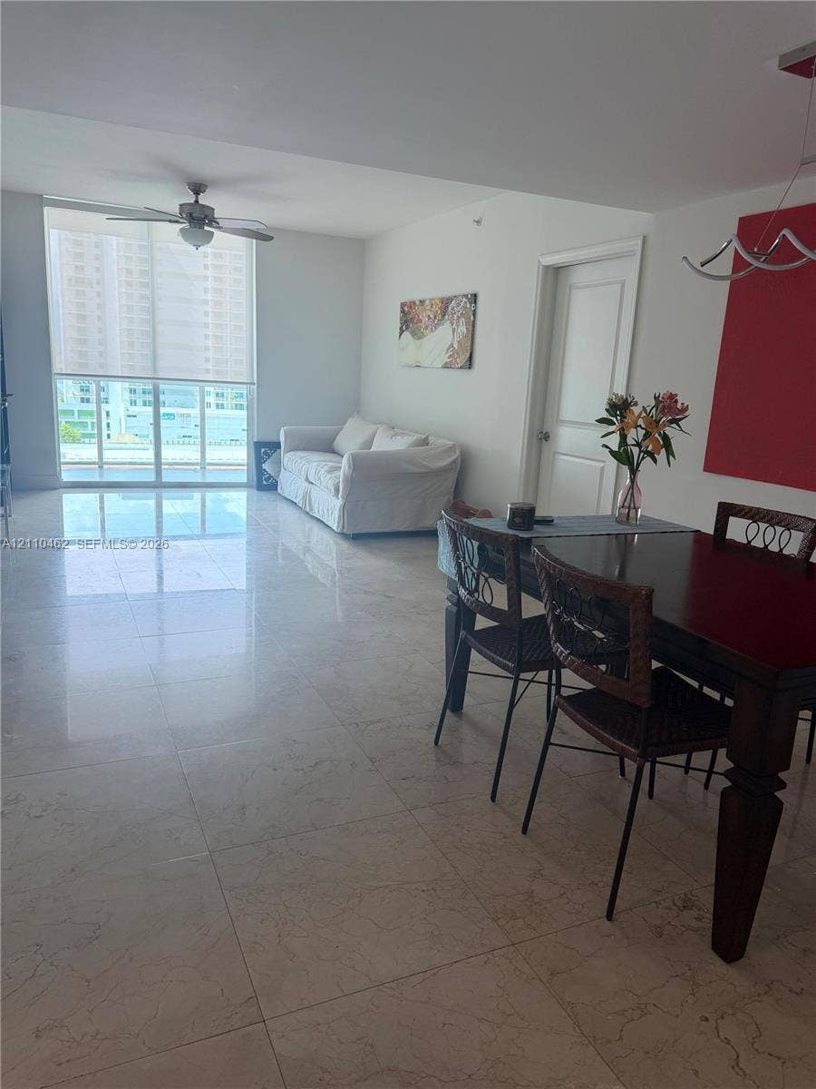 Open-concept interior featuring large-format tile flooring, floor-to-ceiling glass sliding doors, ceiling fan, and modern multi-bulb hanging light fixture