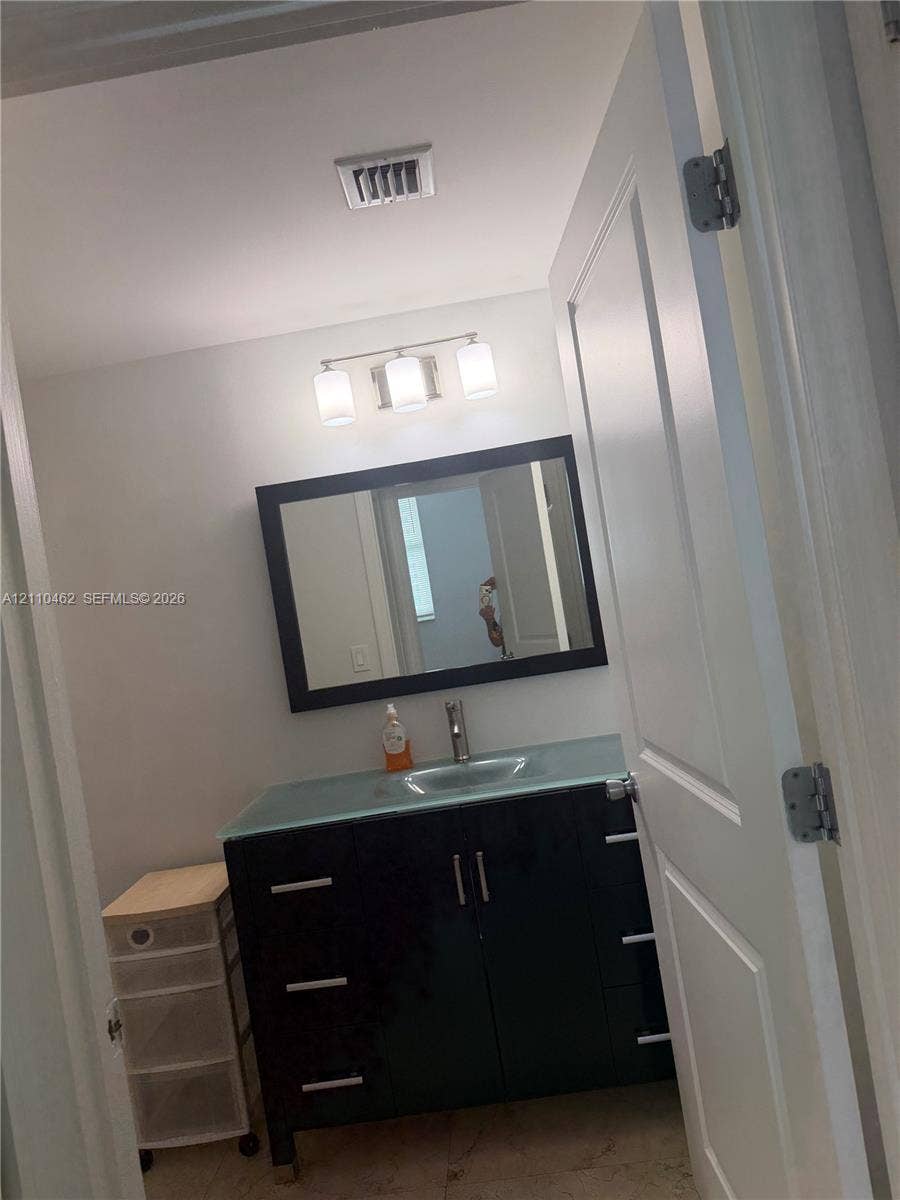 Dark wood-finish vanity featuring a light-toned countertop with integrated sink, rectangular mirror with a dark frame, and a three-light vanity fixture