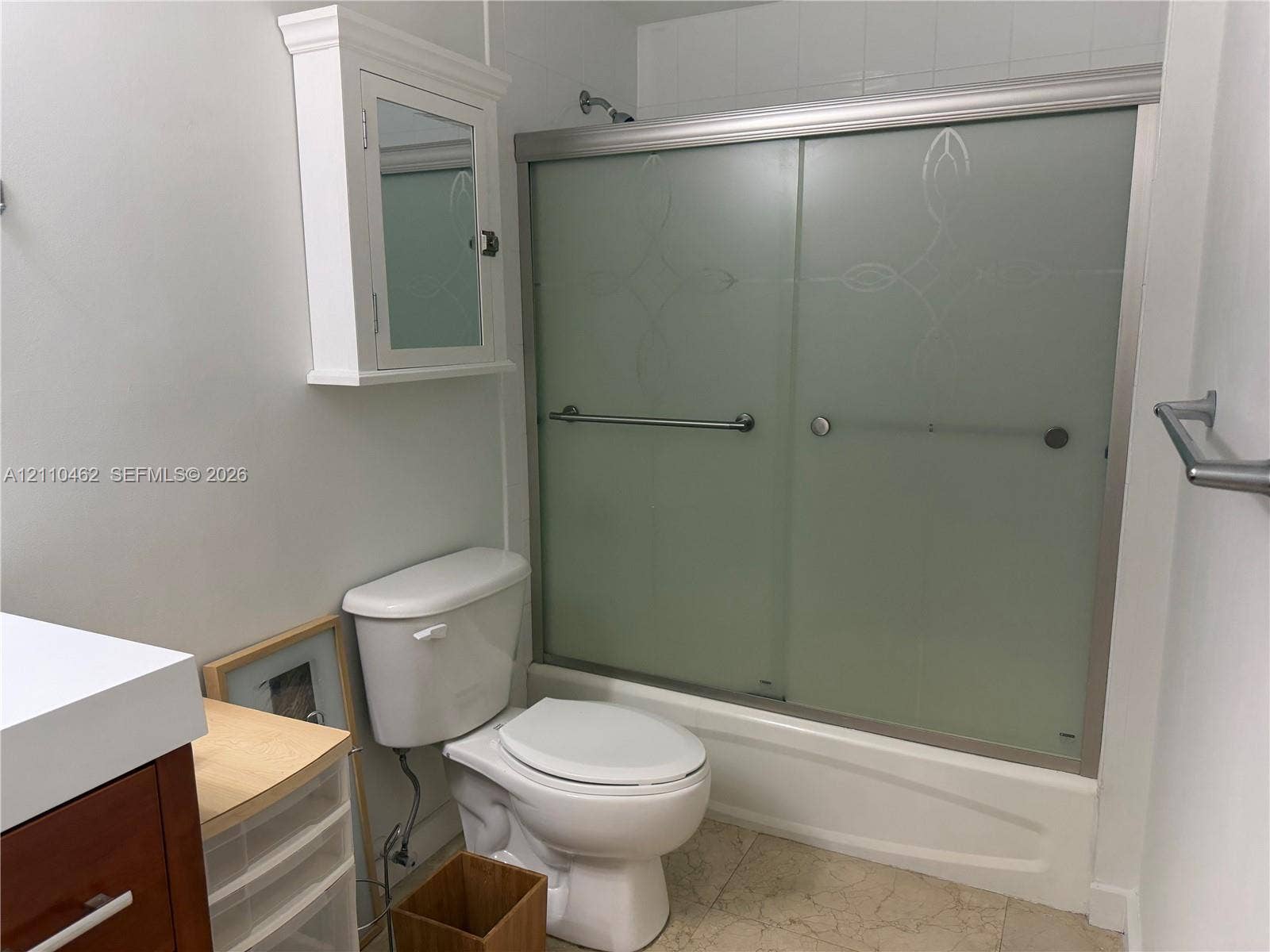 Bathtub with frosted sliding glass doors, wall-mounted medicine cabinet, white toilet, and tile flooring