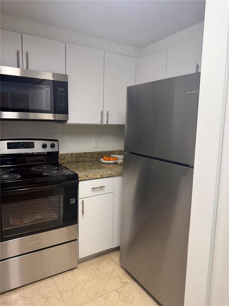 Kitchen featuring white cabinetry, stone-finish countertops, stainless steel appliances, and tiled flooring