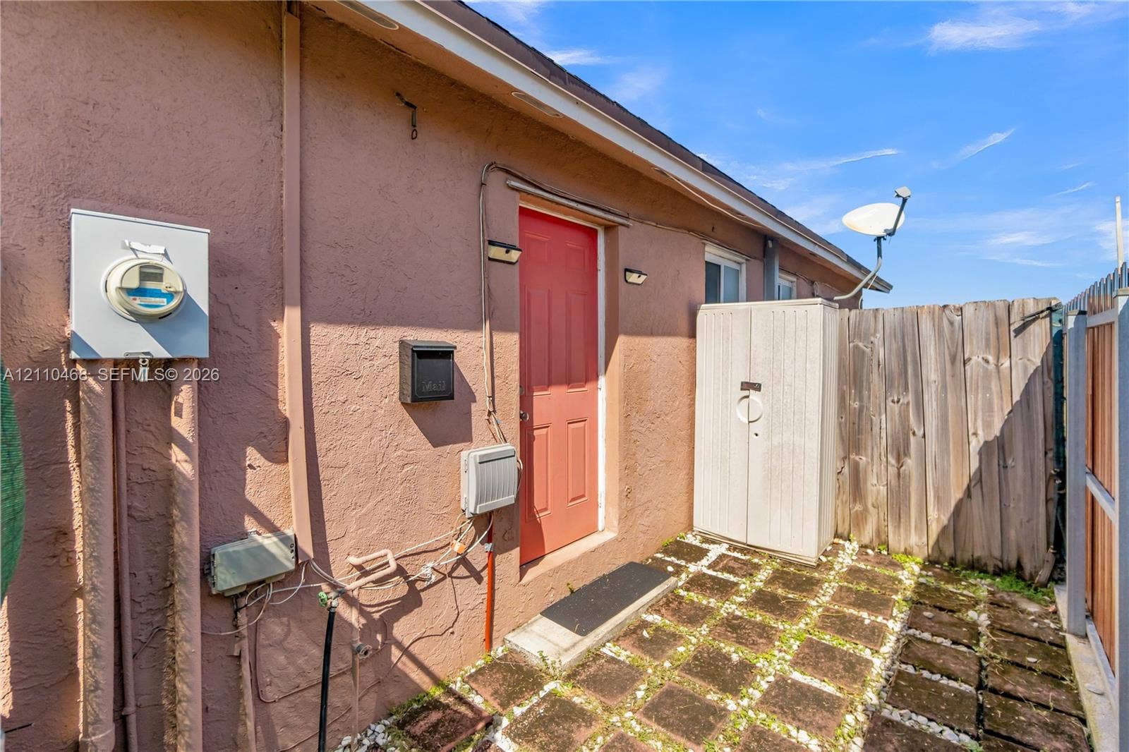 Stucco exterior featuring a solid core entry door, paver patio, and wood privacy fencing