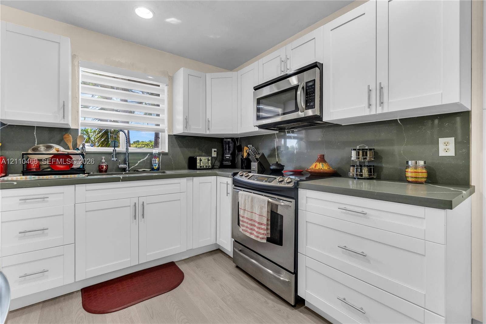 Kitchen featuring white shaker-style cabinetry, solid-surface countertops, full-height backsplash, stainless steel appliances, and wood-finish flooring