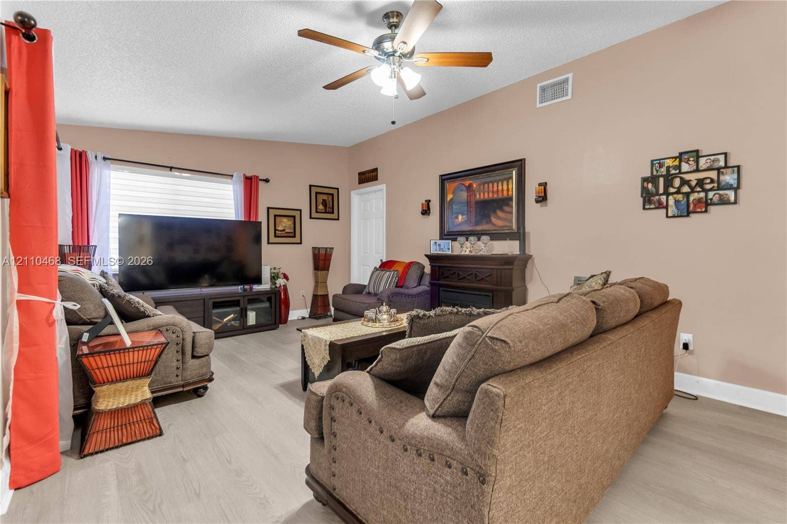 Living area featuring wood-finish flooring, a ceiling fan with integrated lighting, and a built-in decorative mantle