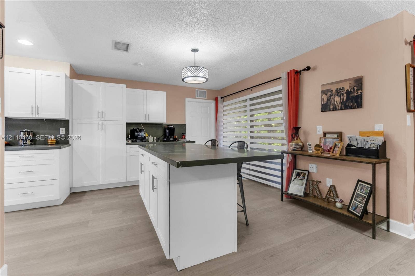 Kitchen featuring white cabinetry, a center island with an integrated countertop, wood-finish flooring, and a drum-style pendant light