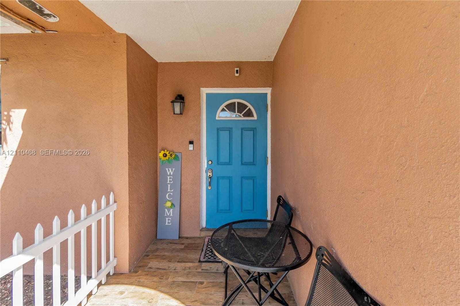 Covered entryway featuring a blue front door with a semicircular transom window, wall-mounted exterior lighting, and wood-finish flooring