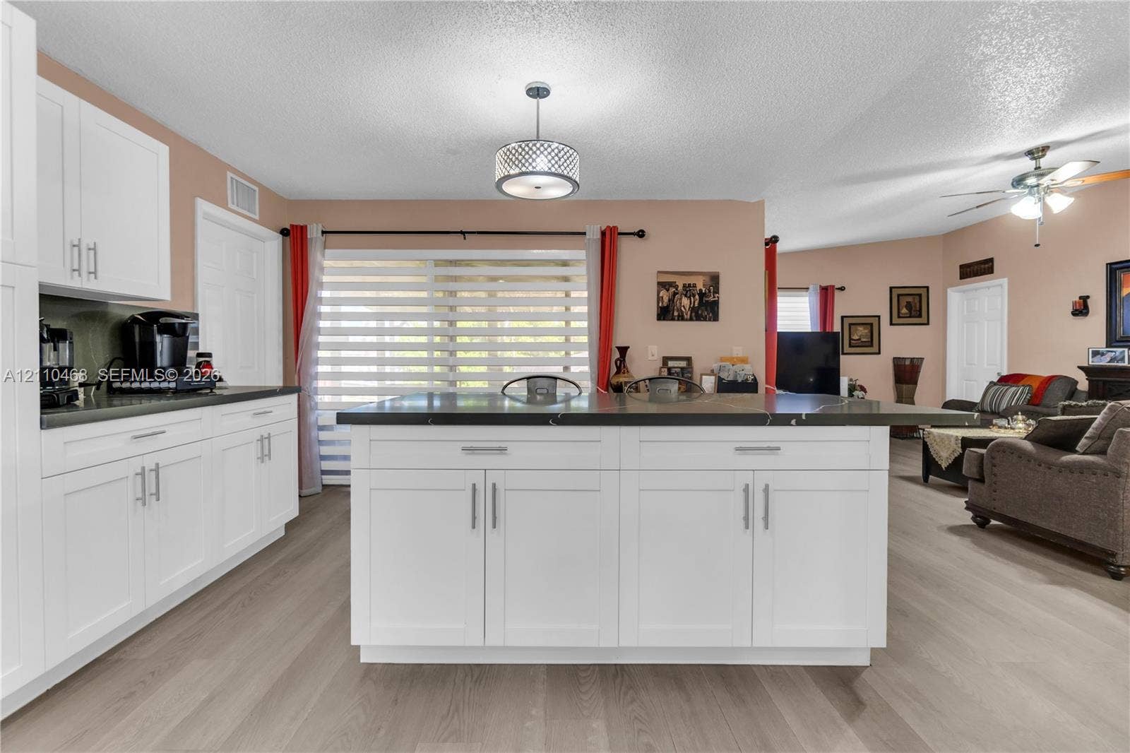 Kitchen featuring white shaker-style cabinetry, a central island with dark stone countertops, wood-finish flooring, and a contemporary drum pendant light fixture