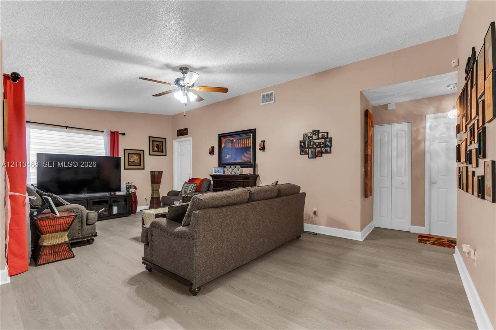 Living area featuring wood-finish flooring, a ceiling fan with integrated lighting, and white six-panel closet doors