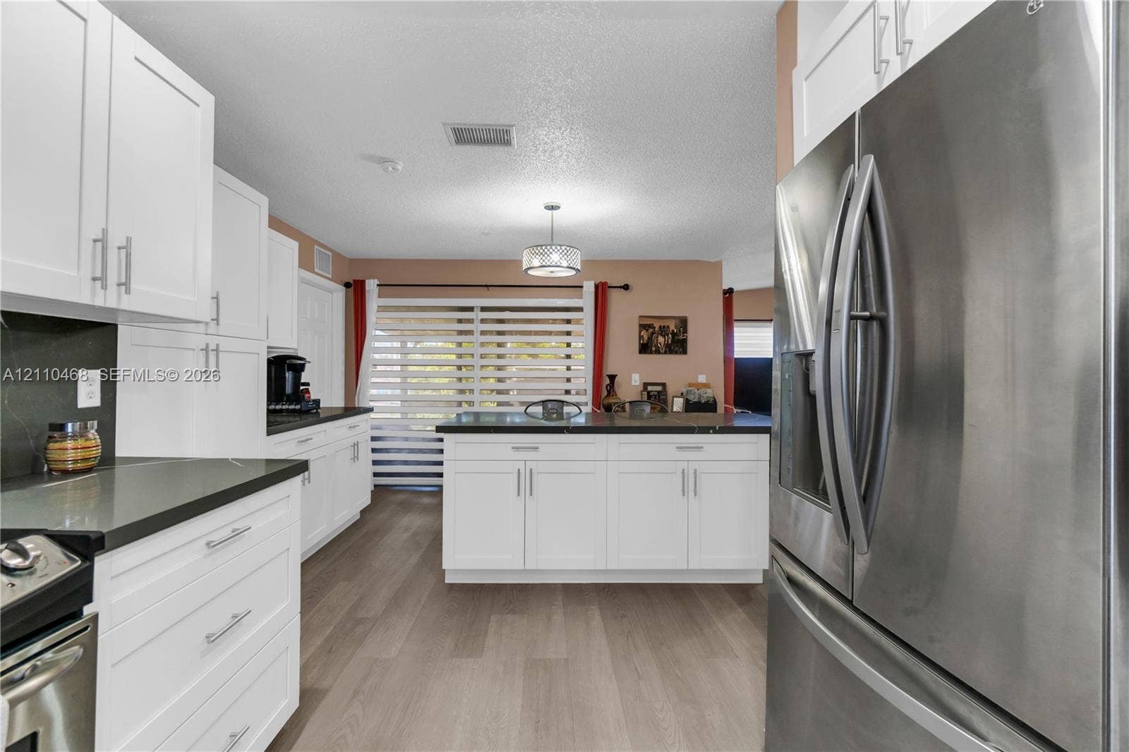 Kitchen featuring white shaker-style cabinetry, dark stone-finish countertops, stainless steel appliances, wood-finish flooring, and a central island