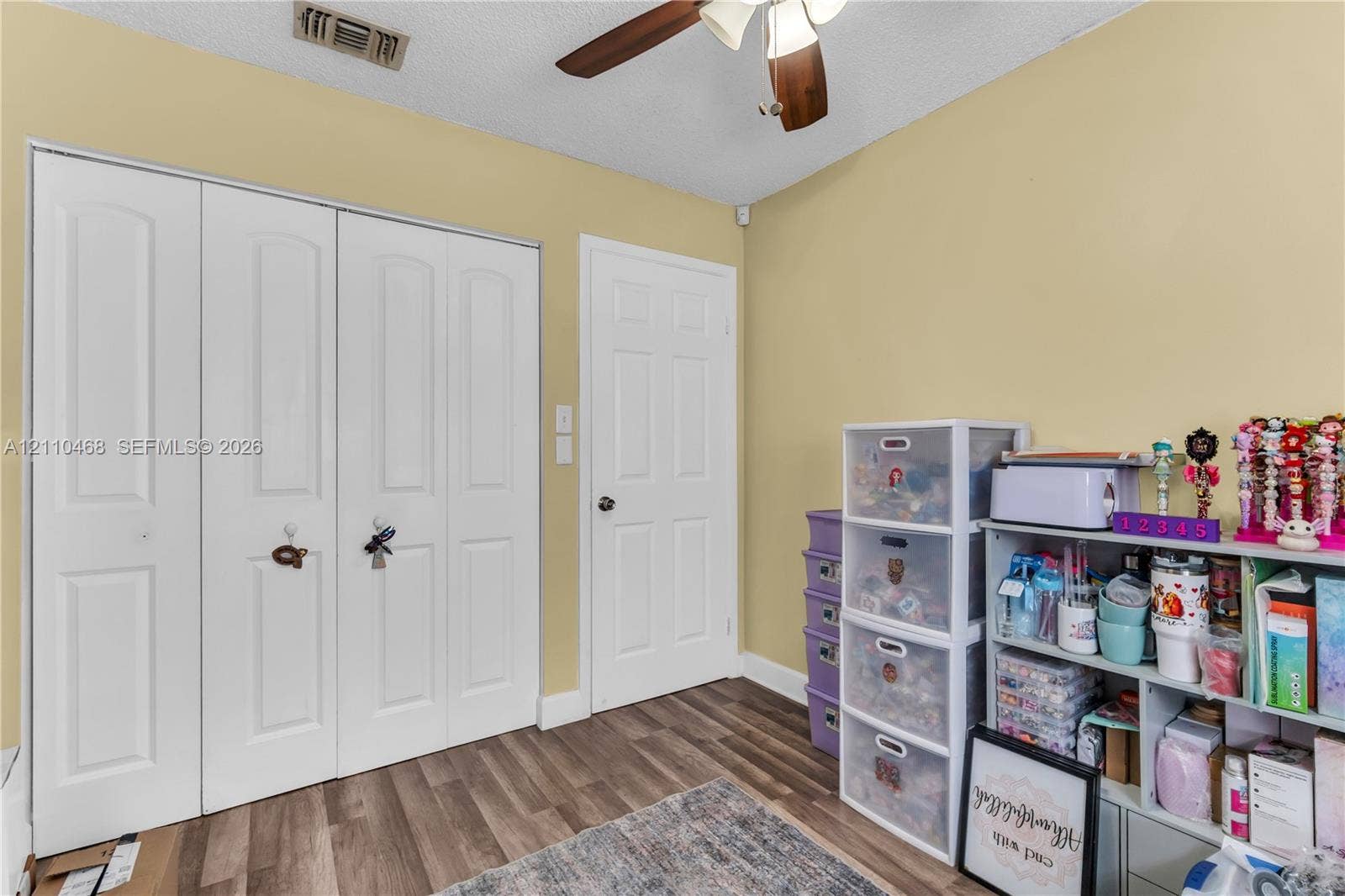 Wood-finish flooring, white multi-panel interior doors, floor-to-ceiling tri-fold closet doors, and a ceiling-mounted light fixture with fan