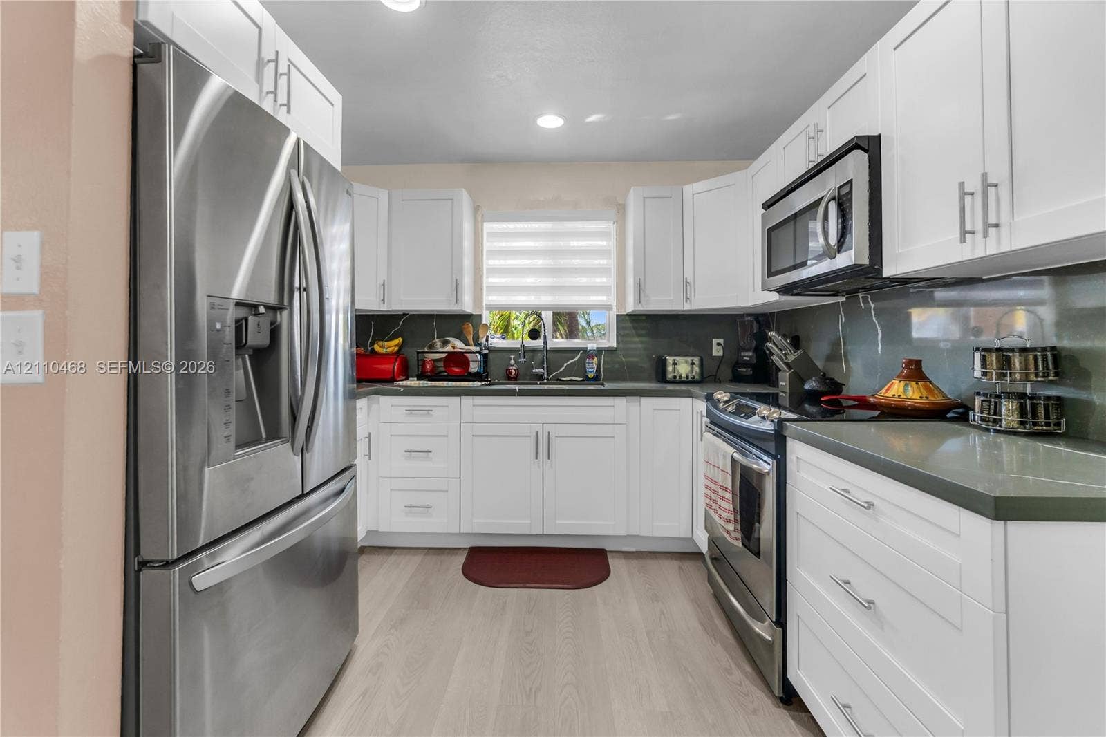 Kitchen featuring white Shaker-style cabinetry, stainless steel appliances, neutral solid-surface countertops, and wood-finish flooring