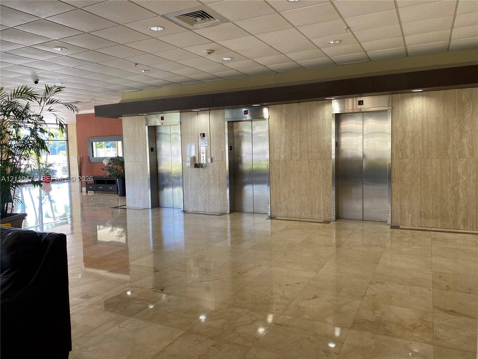 Lobby featuring stainless steel elevator doors, large-format tile flooring, and wall paneling