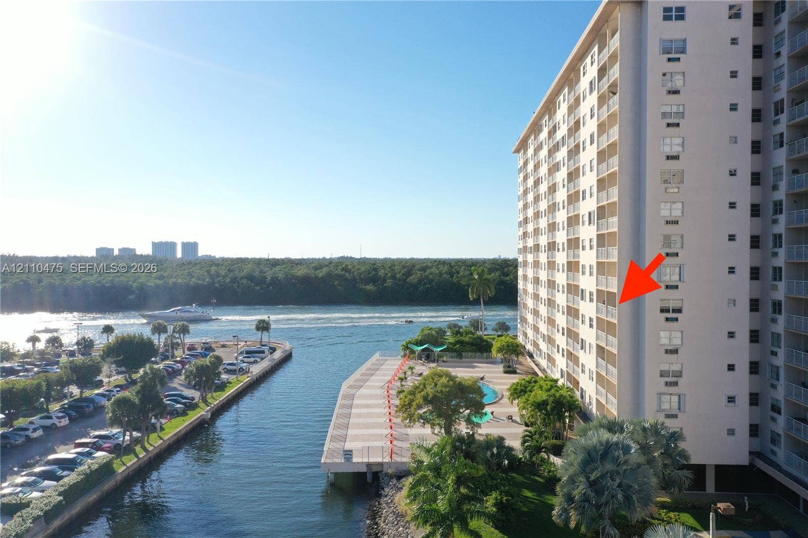 High-rise building featuring private balconies, an outdoor swimming pool, paved waterfront deck, and direct access to the waterway