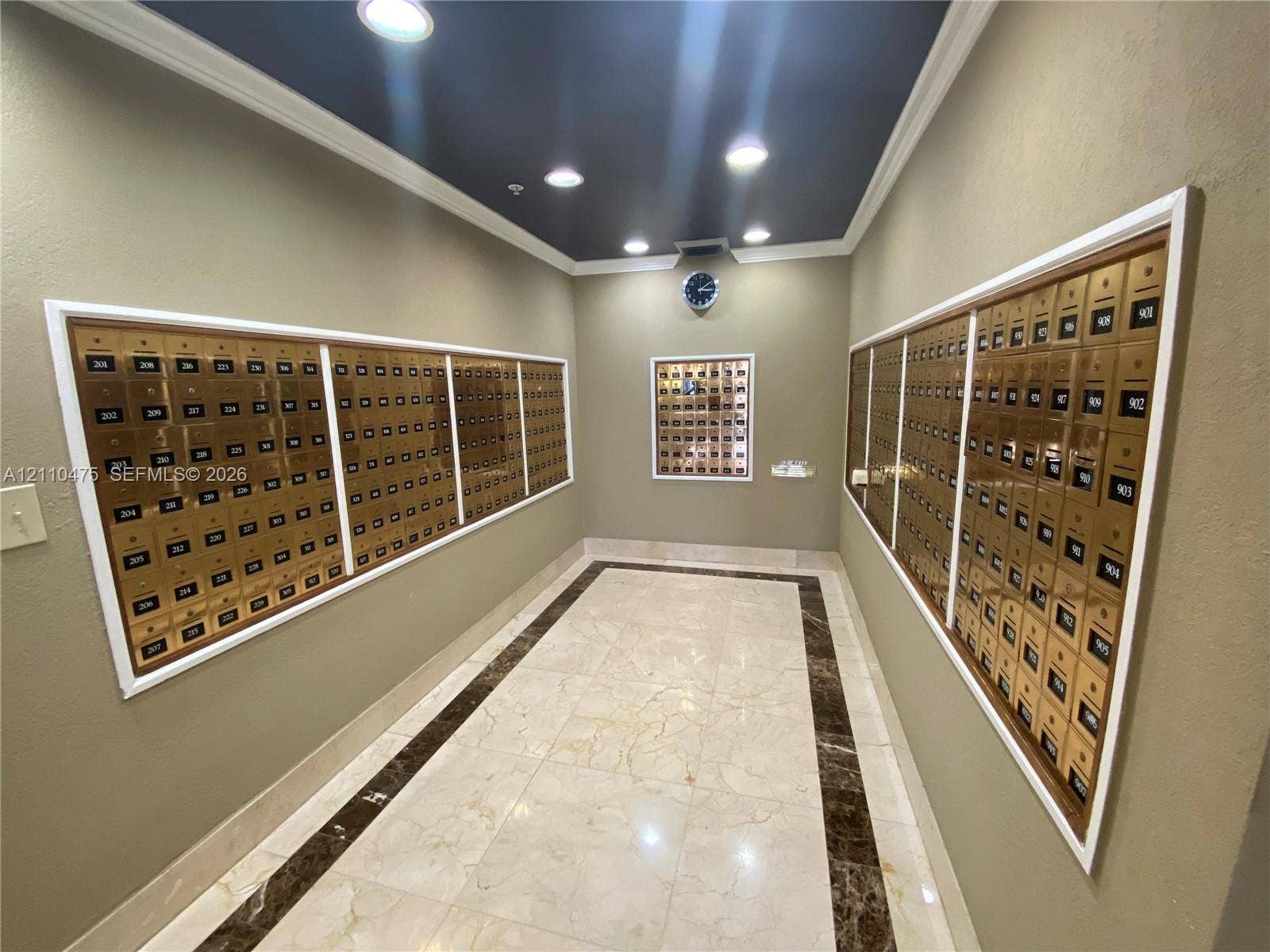 Mail center featuring recessed metal mailboxes, polished tile flooring with contrasting stone-finish border inlay, crown molding, and recessed lighting