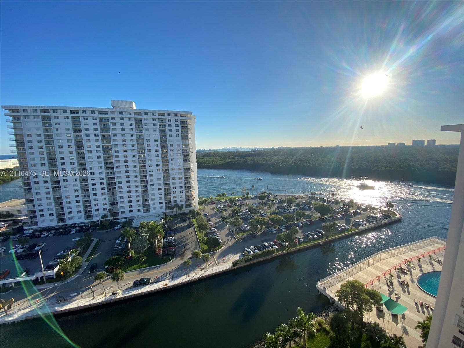High-rise balcony providing an expansive perspective of the coastal waterway, parking facilities, surrounding foliage, and a nearby swimming pool