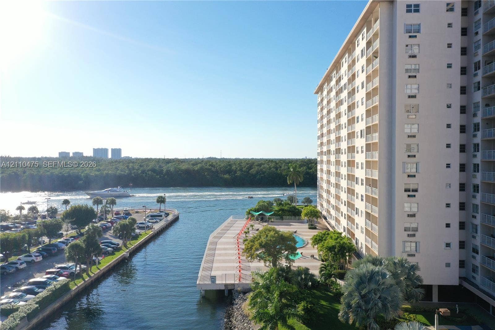 High-rise building exterior with a waterfront pool deck, paved hardscaping, mature palm trees, and canal-front positioning
