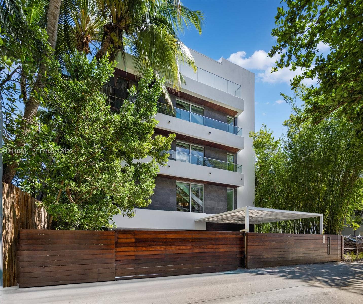 234 Washington Avenue, #D, Miami Beach, FL 33139 Modern multi-story exterior featuring white stucco and dark stone cladding, stacked balconies with glass railings, and a horizontal wood slat perimeter fence