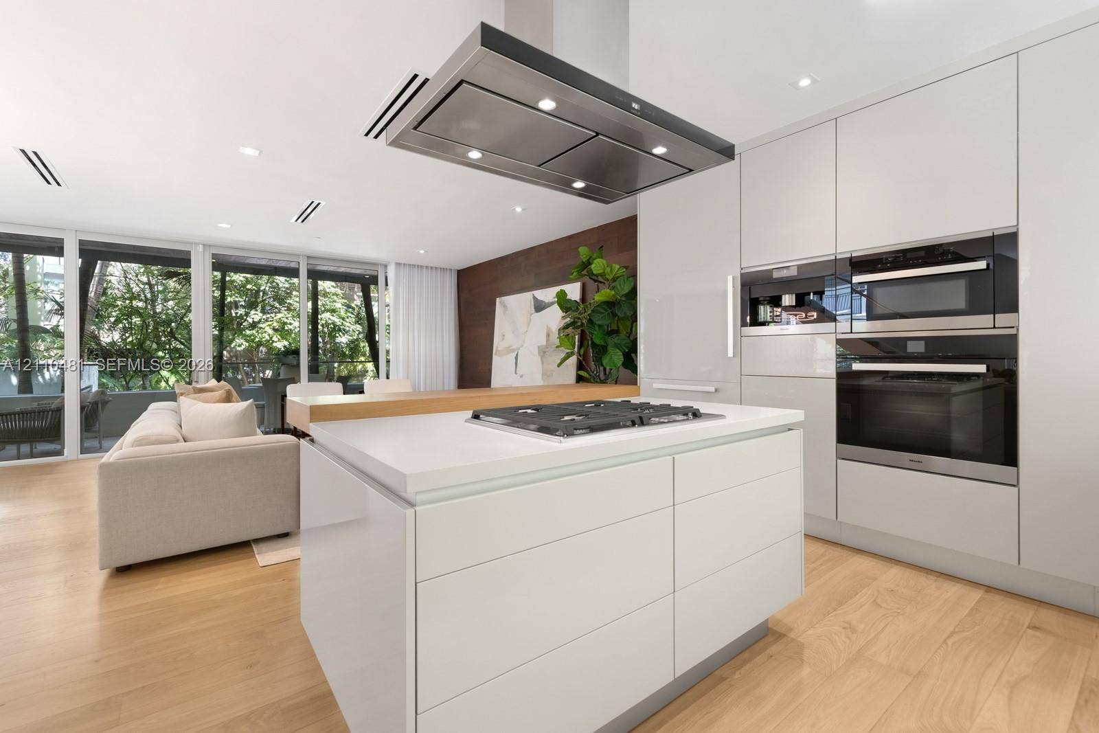 234 Washington Avenue, #D, Miami Beach, FL 33139 Kitchen featuring flat-panel cabinetry, center island with a gas cooktop, built-in wall ovens, stainless steel ceiling-mounted vent hood, and wood-finish flooring