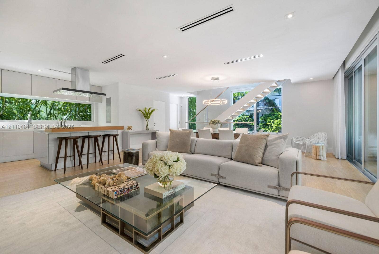 234 Washington Avenue, #D, Miami Beach, FL 33139 Open-concept interior featuring light wood-finish flooring, linear recessed lighting, a modern floating staircase with glass railings, large horizontal windows, and a stainless steel kitchen ventilation hood